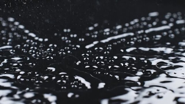 Mesmerizing slow motion macro footage of a pure water drop impacting a black liquid surface creating an elegant crown splash and detailed ripples.