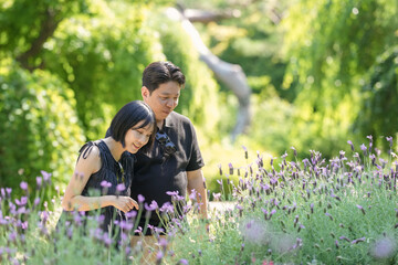 Fototapeta premium A man and woman are standing in a field of purple flowers. The woman is looking at the flowers while the man looks at her. Scene is peaceful and romantic