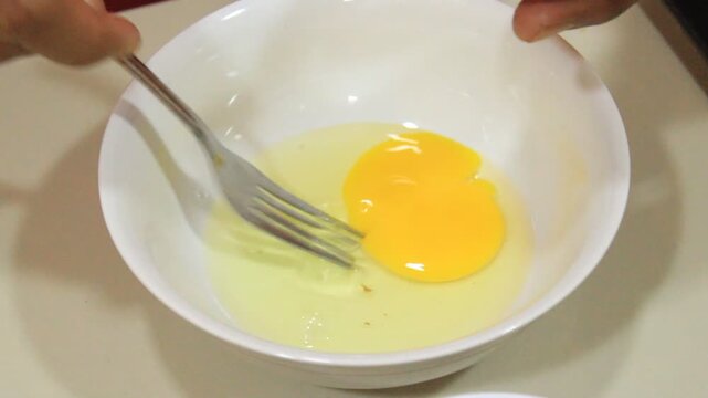 Someone breaks an egg in a bowl. Beat the eggs in a white bowl