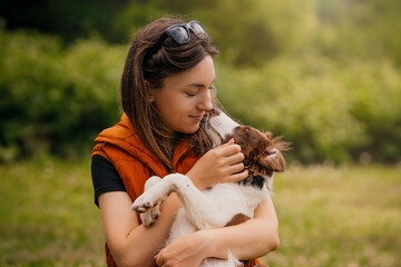Woman Holding Border Collie Puppy in Park. Young woman in an orange vest gently hugs her Border Collie puppy while the dog nuzzles her face in a green park. © kathrineva20