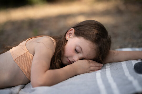 Girl in swimsuit sleeping on towel at beach with closed eyes, peaceful summer childhood relaxation and outdoor leisure with copy space