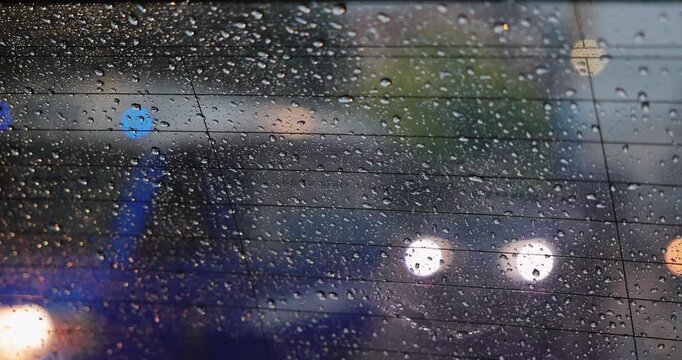 Abstract pattern of rain drops on car window glass with blurred city traffic background. Rainy day weather and sad mood concept. High quality 4K video.