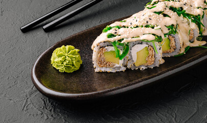 Delicious sushi roll served with wasabi and chopsticks on a black plate
