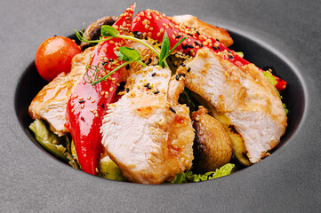 Colorful grilled chicken salad with veggies on a black plate