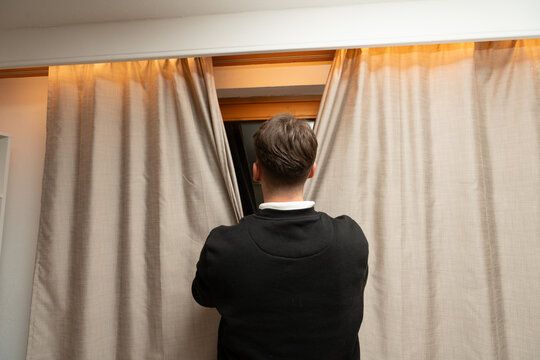 Man peeking through curtains looking out window