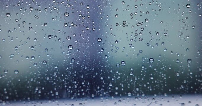 Abstract pattern of rain drops on car window glass with blurred city traffic background. Rainy day weather and sad mood concept. High quality 4K video.