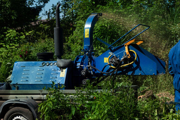 Male Arborist using a working wood chipper machine.The tree surgeon is wearing a safety helmet with a visor and ear protectors.