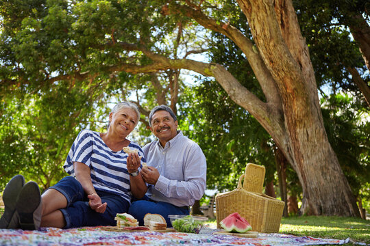 Picnic, smile and thinking with old couple in park together for anniversary, bonding or romance. Basket, eating food and reflection with happy senior people outdoor in nature for retirement wellness