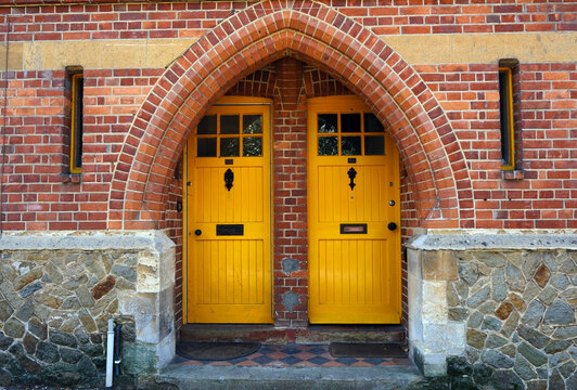 Symmetrical Twin Yellow Doors Beneath a Red Brick Gothic Archway on St Annes Hill, Midhurst, West Sussex