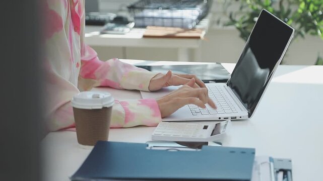 Two financial accountants analysing business spreadsheets on laptop computer, sitting at office desk, looking through paper documents, using calculator working with databases, checking excel tables