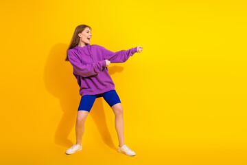 Young woman dancing in a purple hoodie and blue shorts against a bright yellow background for stock advertising