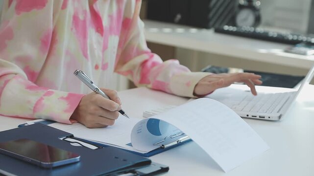 Two financial accountants analysing business spreadsheets on laptop computer, sitting at office desk, looking through paper documents, using calculator working with databases, checking excel tables