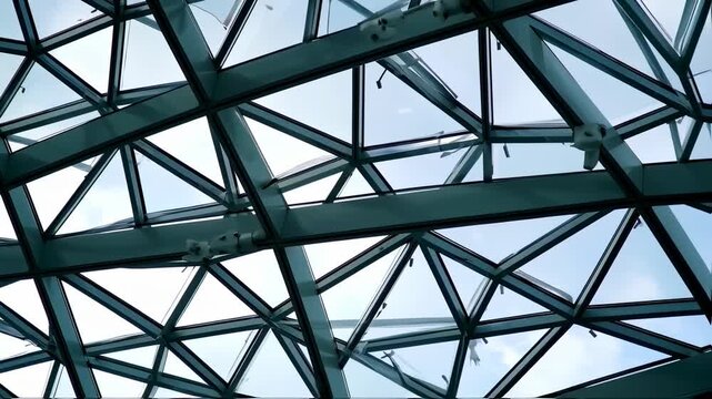 Low angle shot of a geometrically designed glass ceiling with metal supports and a clear sky background