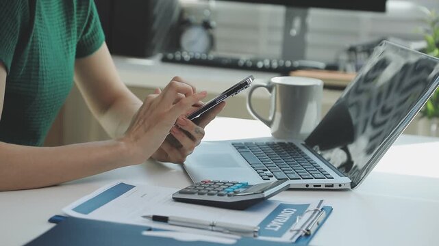 Two financial accountants analysing business spreadsheets on laptop computer, sitting at office desk, looking through paper documents, using calculator working with databases, checking excel tables
