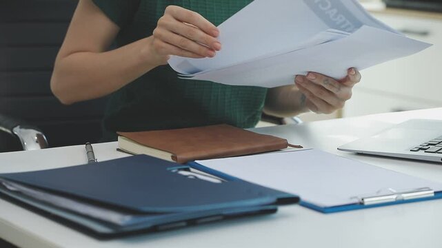 Two financial accountants analysing business spreadsheets on laptop computer, sitting at office desk, looking through paper documents, using calculator working with databases, checking excel tables
