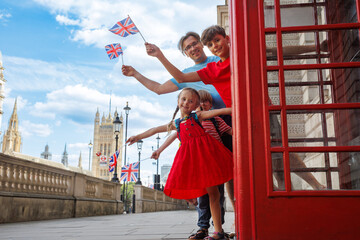 Happy family leans out of a red London booth, waving UK flags