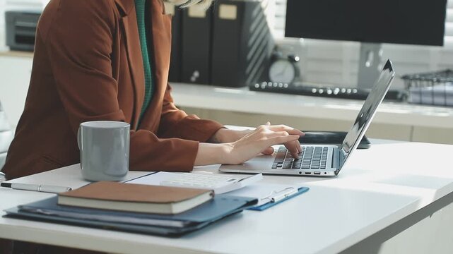Two financial accountants analysing business spreadsheets on laptop computer, sitting at office desk, looking through paper documents, using calculator working with databases, checking excel tables