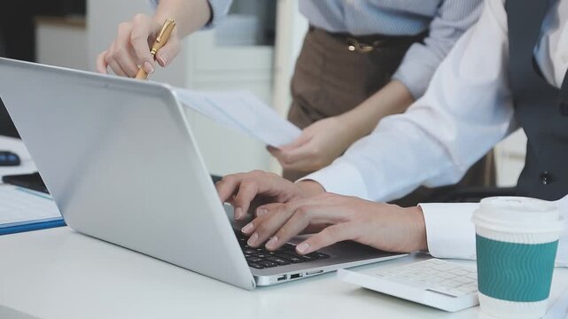 Two financial accountants analysing business spreadsheets on laptop computer, sitting at office desk, looking through paper documents, using calculator working with databases, checking excel tables