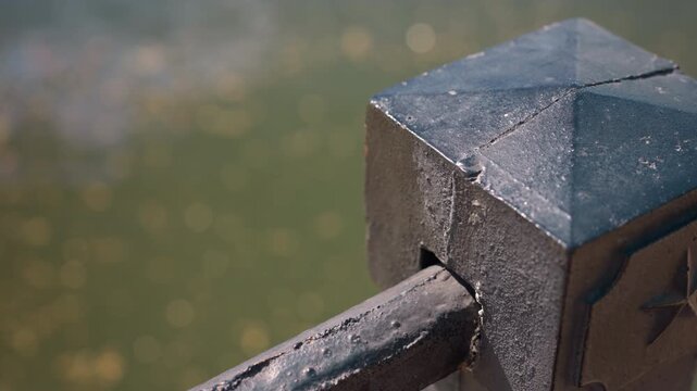 stone railing post with blurred pond background, close-up capture of weathered concrete cap and metal rod, sharp texture and chipped patina, soft bokeh from distant water, warm sunlight highlights,