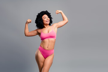 Strong confident woman in pink bikini flexing arms against grey background showing empowerment and...