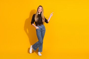 Young woman in casual fashion posing against a bright yellow background smiling and pointing for lifestyle advertising