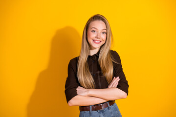 Young woman with blonde hair smiling in casual shirt and jeans against a bright yellow background...