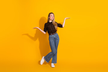 Young woman in casual fashion stands with open arms yellow background smiling posing lifestyle...