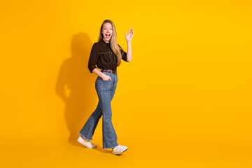 Young woman in casual style smiles and waves against a bright yellow background in a fashion photo...