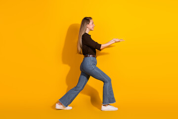 Young woman walking forward with arms extended against a bright yellow background