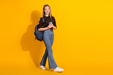 Naklejka premium Young female student with backpack walking against a bright yellow background smiling for fashion lifestyle stock photo