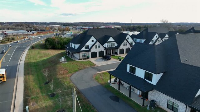 Peaceful American suburban with large modern homes, open green lawns and yellow school bus driving along wide roadway under clear skies. Peaceful autumn sunset. Aerial tracking shot.