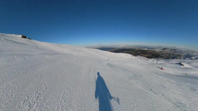 4K action camera POV skiing on a wide, intermediate blue-level slope in Sierra Nevada, Granada, Spain, showcasing a smooth, controlled descent under a pristine blue sky.