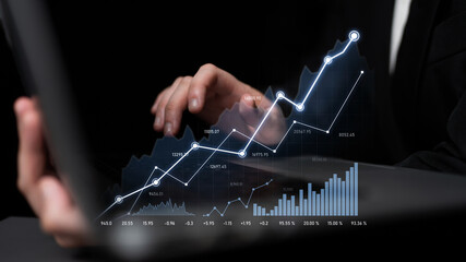 A businessman interacts with a laptop display, analyzing financial data and stock market trends through dynamic charts and graphs against a dark background. Scalp