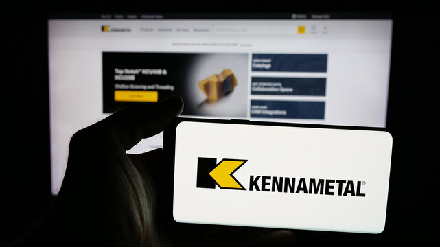 Stuttgart, Germany - 11-26-2025: Person holding mobile phone with logo of US cutting tools company Kennametal Inc. on screen in front of web page. Focus on phone display.