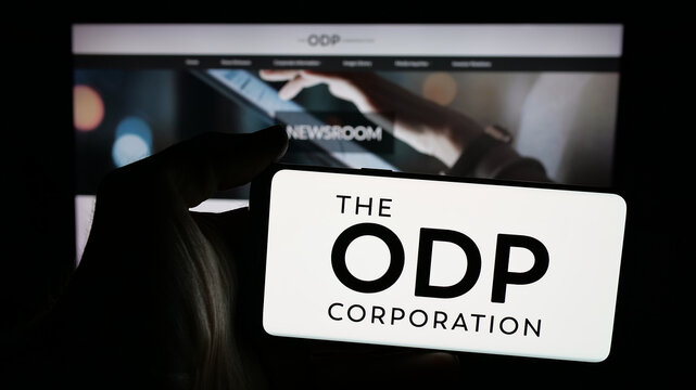 Stuttgart, Germany - 11-26-2025: Person holding mobile phone with logo of US retail company The ODP Corporation on screen in front of web page. Focus on phone display.