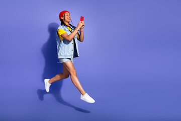Obraz premium Joyful young woman leaps with phone in hand wearing denim streetwear against a violet background