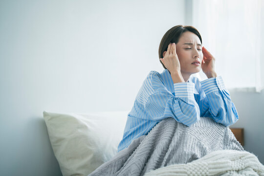 体調不良の女性、彼女は顔を顰めながら両手でこめかみをおさえている