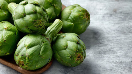 Naklejka premium Fresh artichokes on a wooden board with stone background.