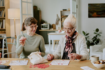 Caucasian middle aged woman and Caucasian senior woman playing board game together at table, both smiling and interacting with game pieces, enjoying leisure activity indoors