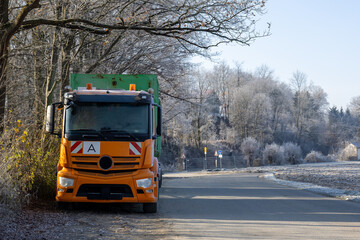 Orange truck parked on a rural frosty roadside near trees, illustrating transport, winter weather conditions and roadside infrastructure