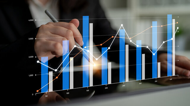 A focused business professional uses a pen to analyze modern graphs and charts, showcasing data trends, growth, and financial metrics in a contemporary office setting. Scalp