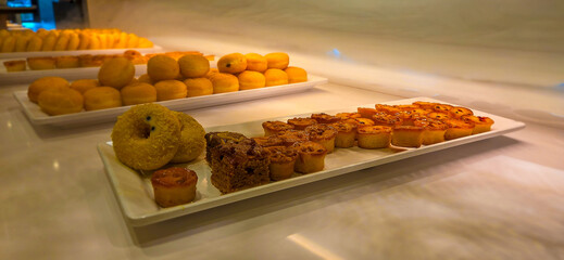 Assorted pastries and donuts displayed on white trays in a bakery.