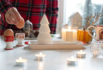 Candle light with Christmas decoration atmosphere while hand putting egg into the egg cup, with festive ambiance decorated on table.