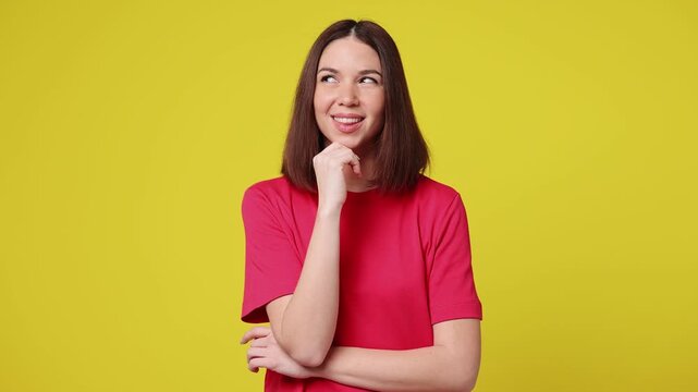 Young Caucasian woman she wear pink t-shirt casual clothes look around think dream put hand prop up on chin lost in thought and conjectures isolated on plain yellow color background. Lifestyle concept
