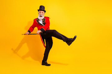 Joyful veteran circus performer in a red coat dances with a cane against a bright yellow background