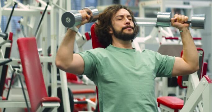 Deltoid workout with dumbbells. Slow motion 4k footage of a Caucasian man during gym workout. Seated dumbbell press for deltoids.