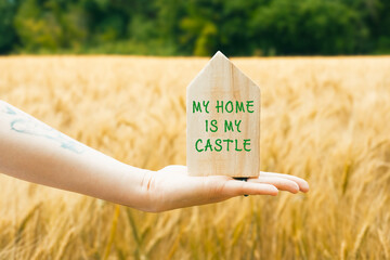 Hand holding wooden house sign with inspirational quote in golden wheat field landscape