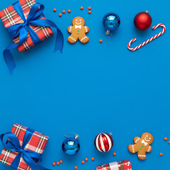 Fototapeta premium Christmas flat lay with gingerbread man, gift box, and ornament on blue