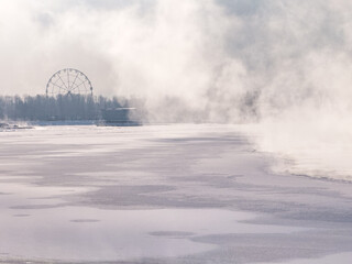 City in dense fog over a river during a late winter morning. Winter landscape