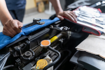A close-up view of a young man holding a wrench as he checks and maintains his car engine by...